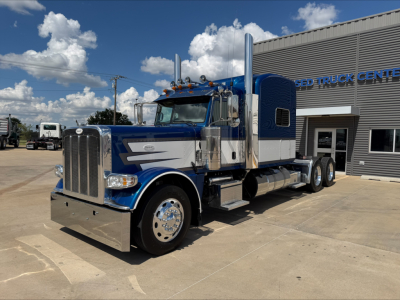Peterbilt 389 conventional sleeper truck in blue and white parked outside a truck center.