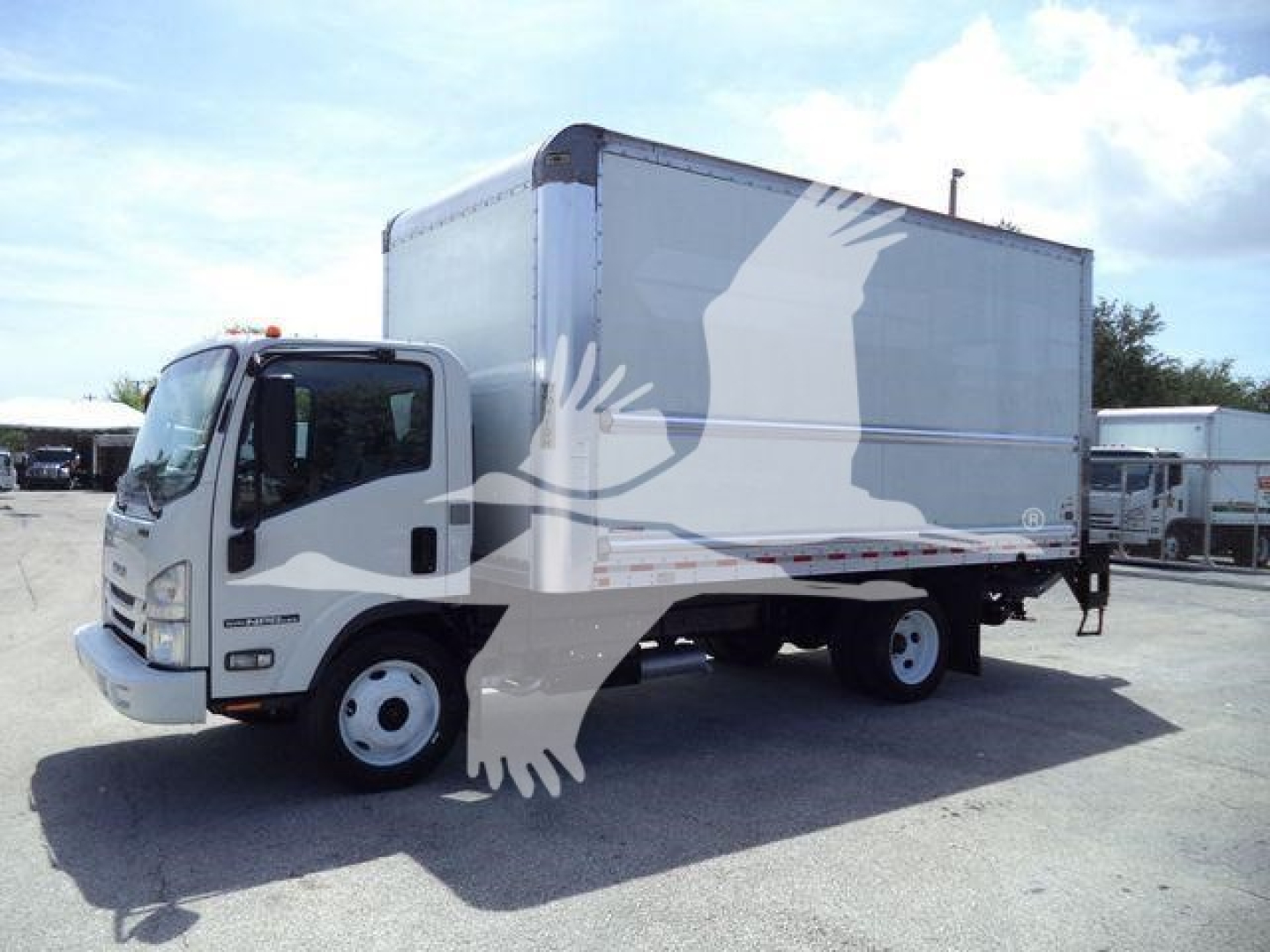 Isuzu NPR-HD box truck in a used status with a large box cargo area; cab shows Isuzu badge and front grille, surrounding lot with other similar trucks.