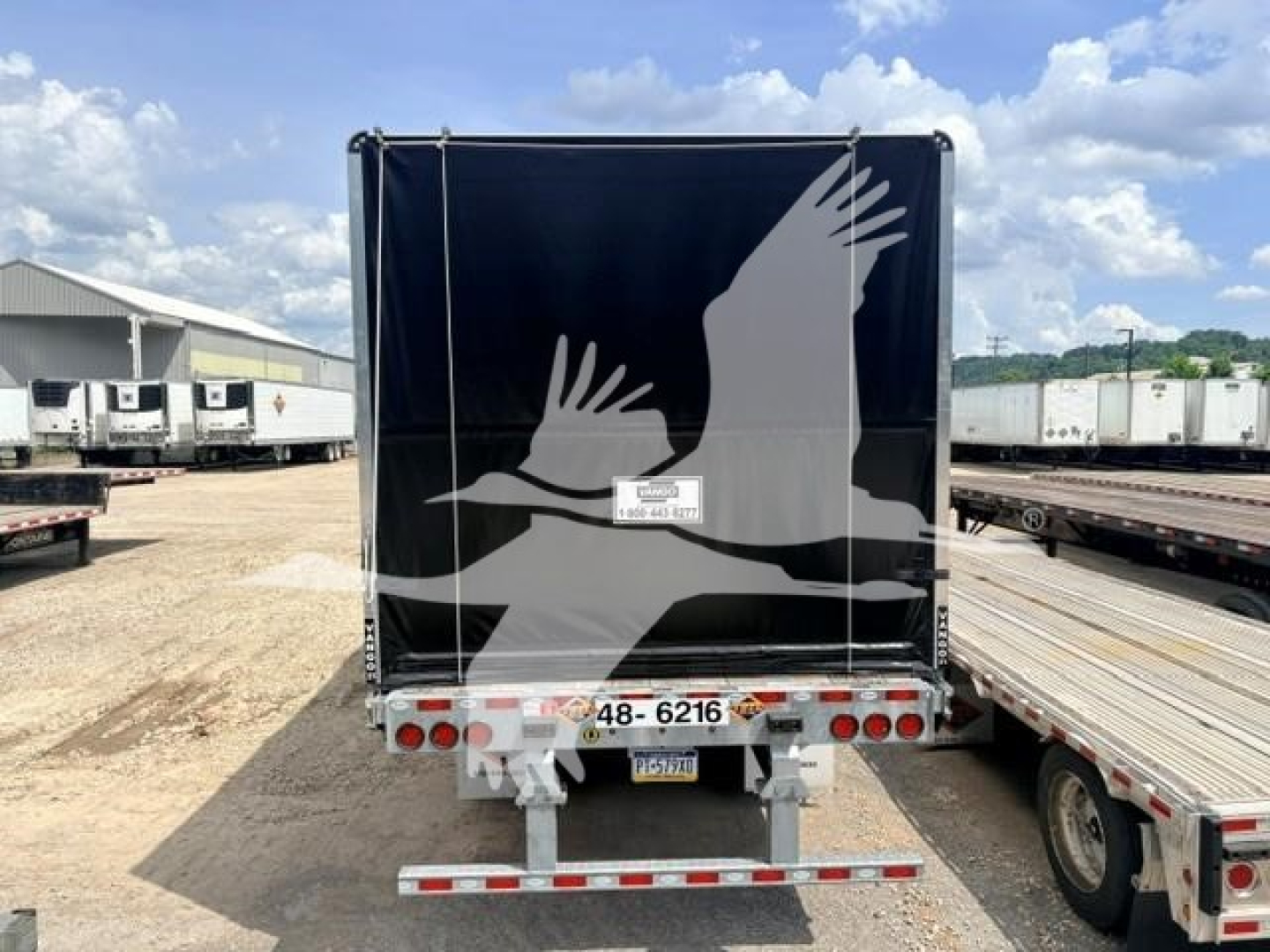 Curtainside trailer back view showing black galvanized flat air slider with white winged graphic and rear lights.