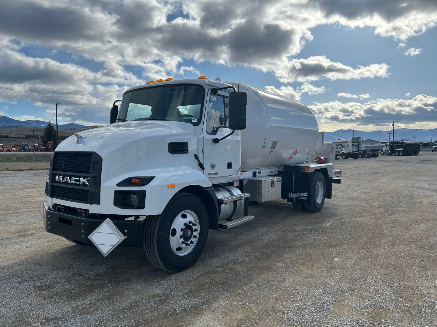 White 2026 Mack MD7 vacuum/ tanker truck in a parking lot, front-left view, displaying Mack grille, cab steps, amber clearance lights, and cylindrical tank with safety decals.