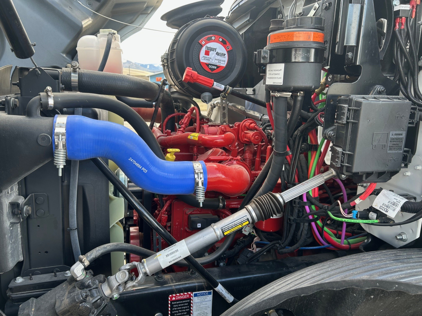 Mack MD7 engine bay showing blue radiator hose, red turbo/intercooler components, black wiring harnesses, and engine accessories.
