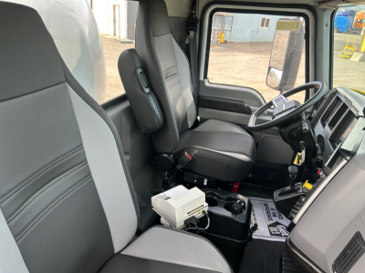 Interior of a new 2026 Mack MD7 truck cab showing driver and passenger seats, steering wheel, and dashboard with gear selector and control modules.