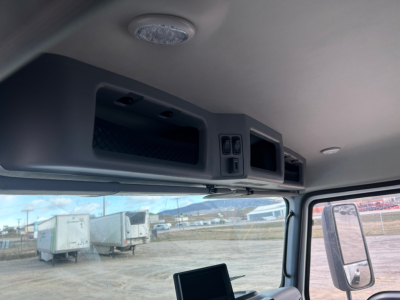 Cab interior of a 2026 Mack MD7 truck showing overhead console with compartments and controls, windshield view, side mirror.