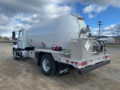 Semi truck rear view showing propane/tank with diamond hazard placard and rear toolbox area.
