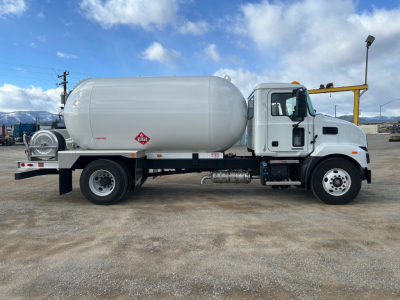 Truck side view showing large cylindrical propane or liquid tank mounted on chassis with Mack MD7 cab in white. Tank has hazard placard and labels visible on side.