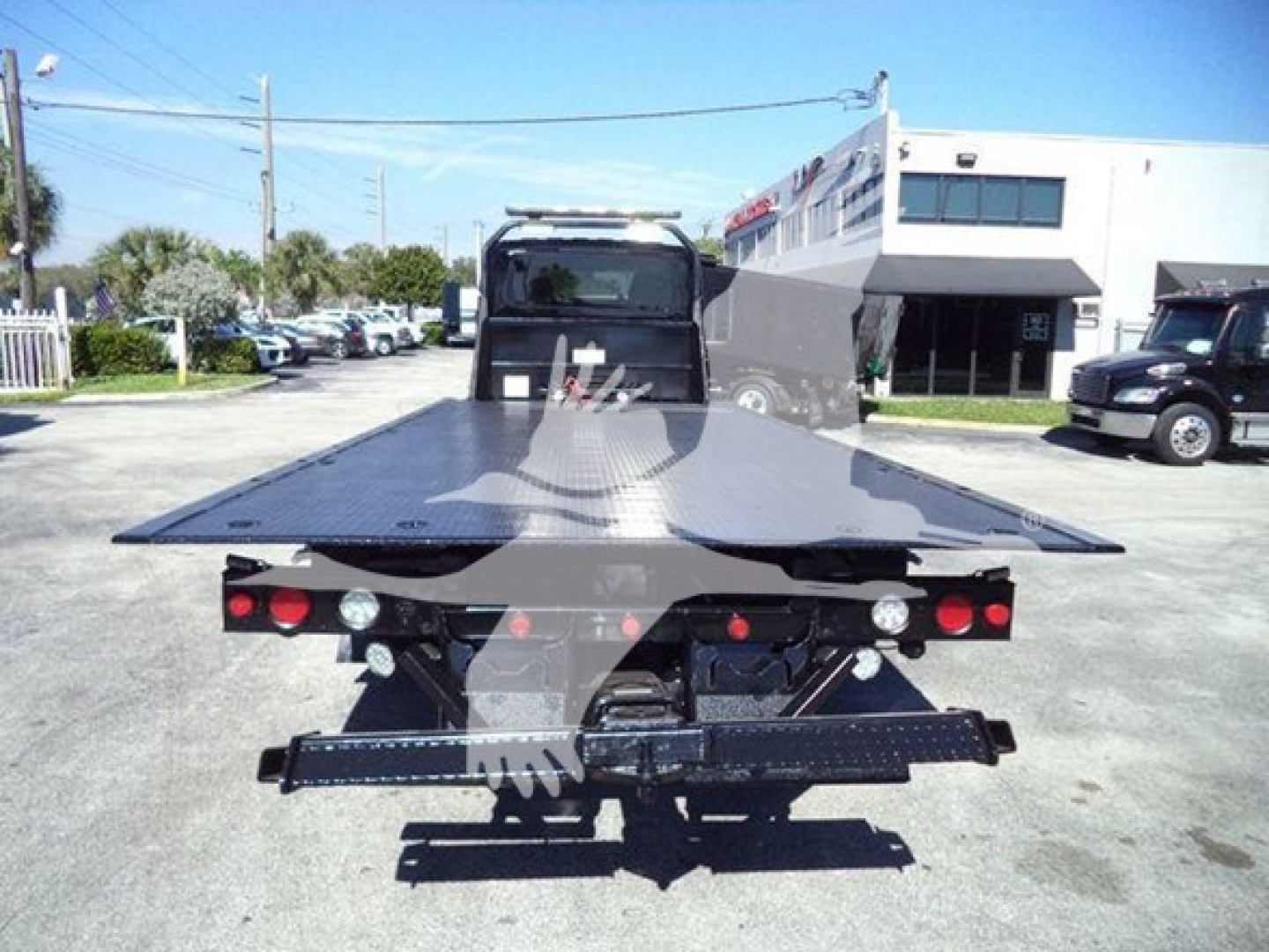 Flatbed tow truck bed with hydraulic rear, MV International rollback truck profile from rear showing platform and taillights.