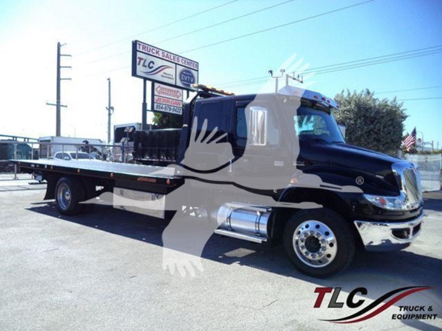 Truck bed tow truck showing International MV with rollback flatbed and chrome fuel tanks.