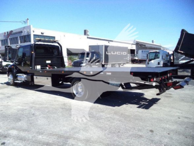 Flatbed rollback tow truck with a Lucid generator and cab in background. Side view shows long flatbed and rear wheel, some equipment and controls visible.