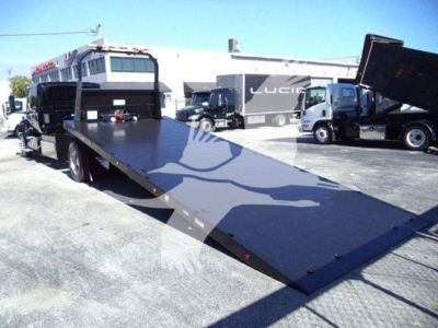Truck rollback bed on 2022 International MV with flatbed ramp and nearby equipment at a lot.