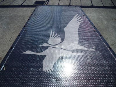 Truck bed platform with a large white bird graphic (likely a crane) on a diamond-plate steel surface; no legible alphanumeric text aside from the graphic