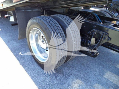 Truck rear axle and dual wheels with suspension components visible under a rollback bed.