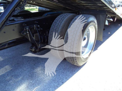 Truck chassis with dual rear wheels and suspension components visible under a rollback bed.