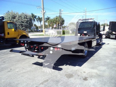Flatbed rollback tow truck shown from rear left side with platform extended.