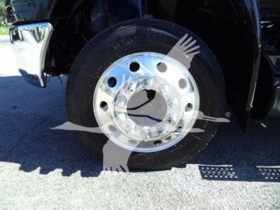 Truck wheel and tire on a rollback International MV showing steel wheel with lug nuts and tire sidewall text.