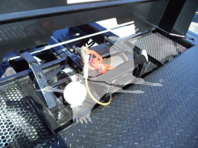 Winch/strap mechanism on a roll-back tow truck bed showing hydraulic winch with white round motor and red wiring cover.