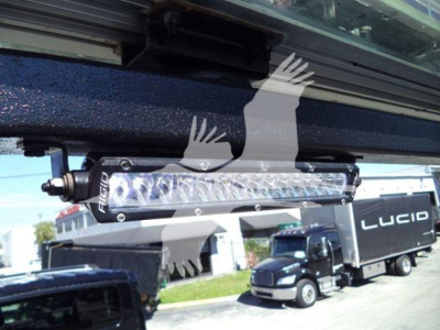 Light bar mounted under truck cab showing LED light bar with brand 'FUEL' on housing, against a rollback truck in background.