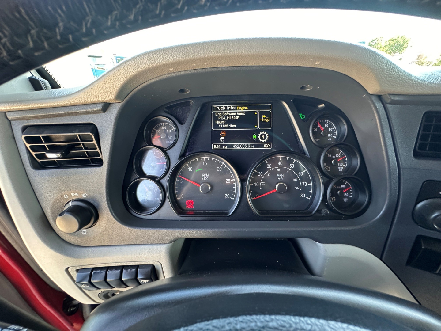 Truck dashboard view of a 2021 Peterbilt 579 with illuminated gauges and a central TFT display showing truck info and a red hazard button visible.