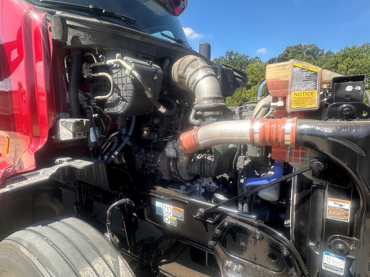 Peterbilt 579 engine bay with hoses and components visible; turbocharger intake and various labels on yellow warning stickers.