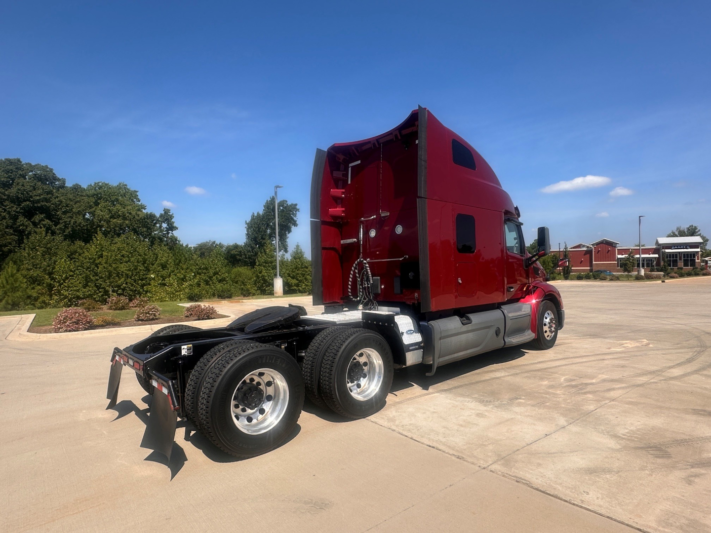 Peterbilt 579 truck tractor from rear-quarter view showing dual rear axles and red sleeper cab with chrome fuel tanks and fifth-wheel area.
