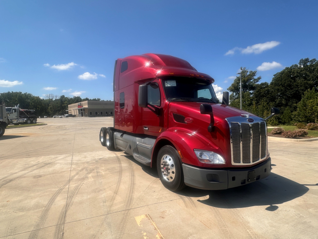 Peterbilt 579 tractor in red with sleeper cab, front grille, and chrome bumper in a parking lot.
