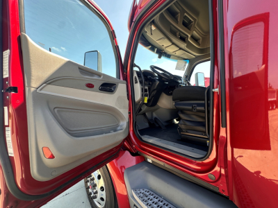 Truck cab interior of a red 2021 Peterbilt 579 with open driver door showing beige interior, dashboard, steering wheel, and entry steps.