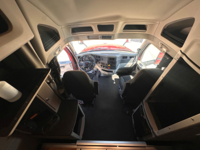 Truck cab interior view from rear toward the dash showing driver and passenger seats, dashboard, steering wheel, and overhead compartments.