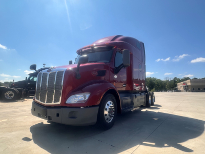 Peterbilt 579 conventional sleeper truck in a parking lot, maroon cab with chrome grille and wheels.