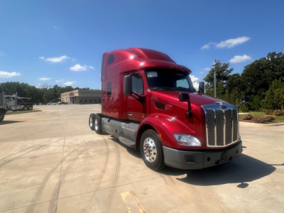 Peterbilt 579 tractor in red with sleeper cab, front grille, and chrome bumper in a parking lot.