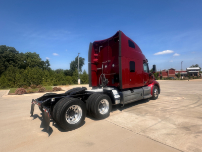 Peterbilt 579 truck tractor from rear-quarter view showing dual rear axles and red sleeper cab with chrome fuel tanks and fifth-wheel area.