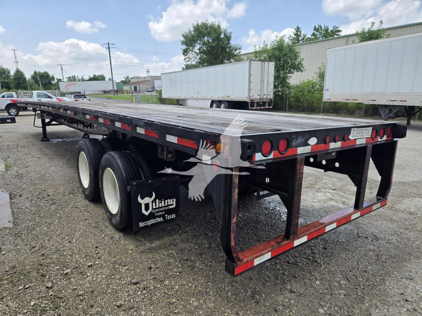 Flatbed trailer showing triple-axle rear with black frame and red/white reflective tape, Viking logo on mudflap area.