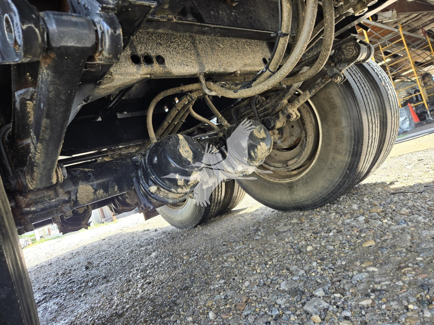 Viking steel flatbed trailer undercarriage showing wheel, suspension, and hydraulic lines; dirt and gravel beneath.