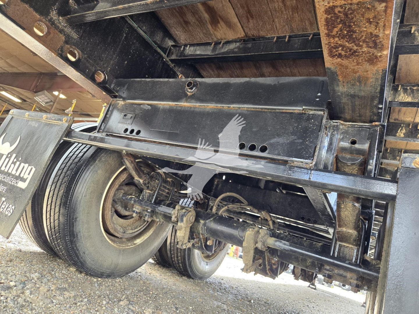 Trailer undercarriage showing steel flatbed frame and suspension with dual wheels. Visible text on mudflap area indicates Viking or Viking-style branding.