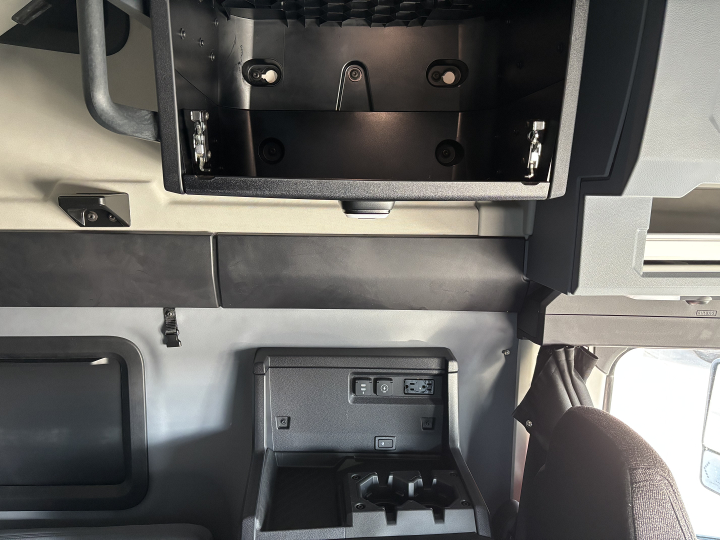 Conventional sleeper truck cab interior showing storage compartments and dashboard area in a Mack PR64T76H. Visible features include overhead storage bay and a small control panel with USB ports.