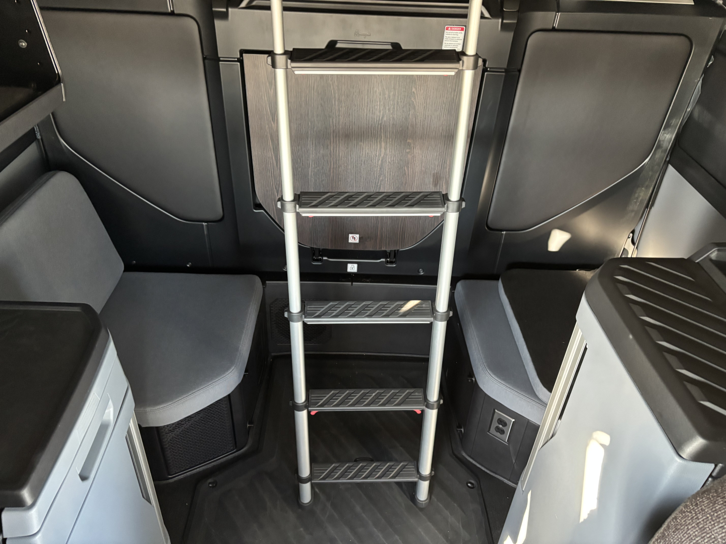 Mack PR64T76H truck cab interior showing metal ladder steps leading to upper area, with seating and storage panels on both sides.