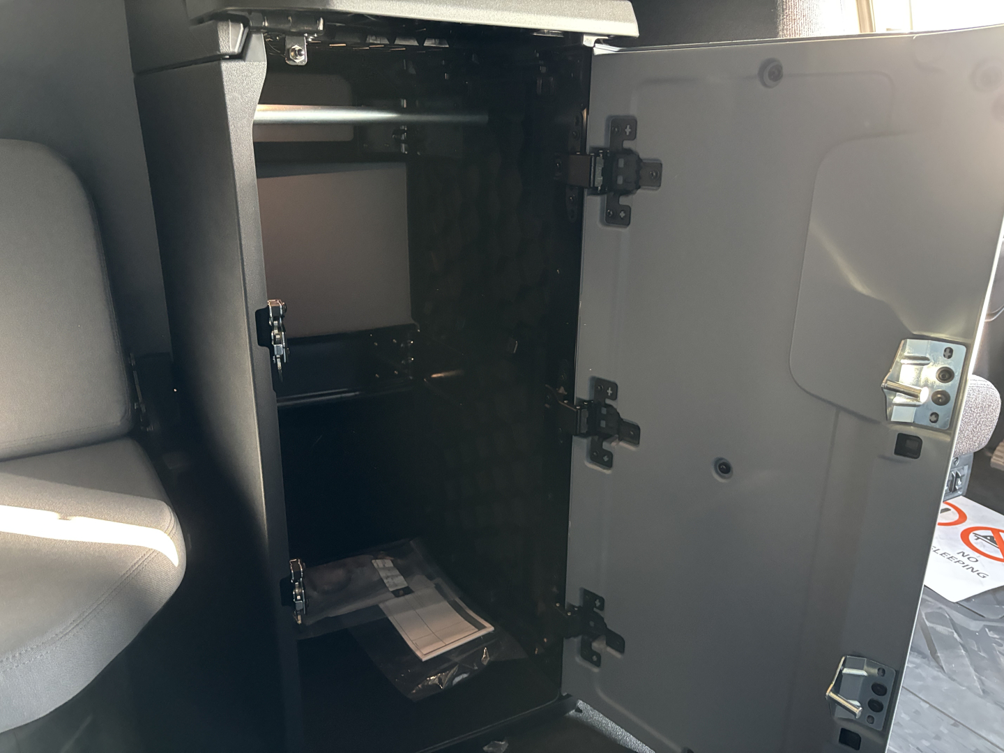 Cab interior of a new Mack PR64T76H truck showing an open storage cabinet with shelves and a small device inside.