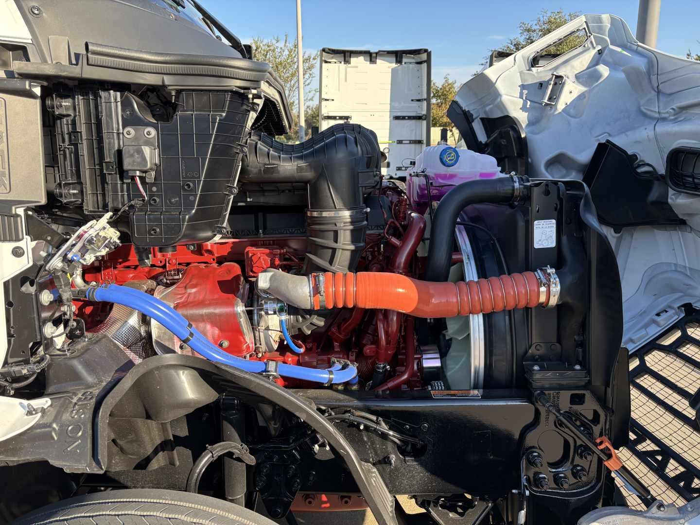 Mack PR64T76H engine bay with red engine block, blue coolant line, and orange high-pressure hose in view.