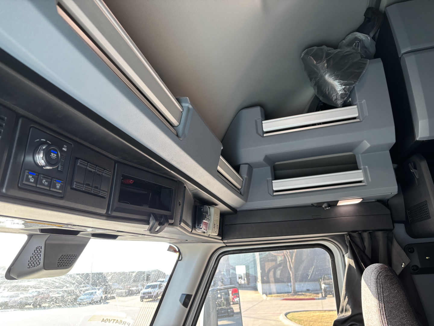 Cab interior of a new Mack PR64T76H truck showing overhead bunk area, storage compartments, and control panel with dashboard elements.