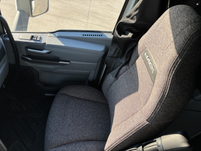 Cab interior of 2026 Mack PR64T76H truck showing gray fabric seat with Mack logo and part of dashboard and door panel.