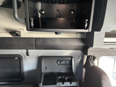Conventional sleeper truck cab interior showing storage compartments and dashboard area in a Mack PR64T76H. Visible features include overhead storage bay and a small control panel with USB ports.