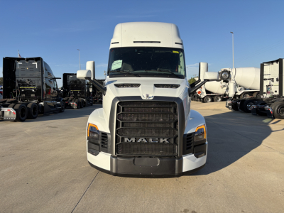 Truck front view showing Mack grille and front bumper. Hood and headlights visible; large black grille with MACK letters at center. Side mirrors and other trucks in background.