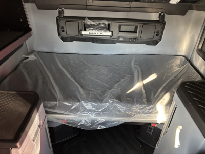 Mack PR64T76H cab interior view showing bunk area with plastic-covered mattress, overhead control panel, and storage shelf.