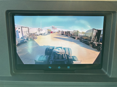 Truck cab display showing a daytime view of a truck dealership lot with multiple trailers and tractors lined up.