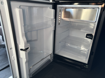Fridge compartment of a new Mack PR64T76H sleeper truck showing interior with shelves, freezer and door storage.