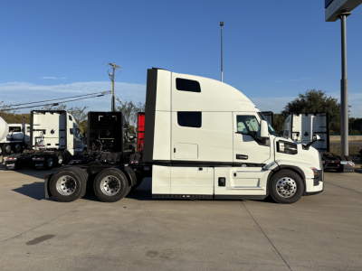 Tractor-trailer truck side view showing a white Mack PR64T76H sleeper cab with multiple rear axles and a flatbed chassis.