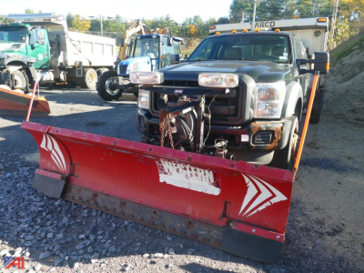 Ford F-550 Super Duty pickup with front plow attached, black cab, red snow plow blade, truck in a yard with other machinery.