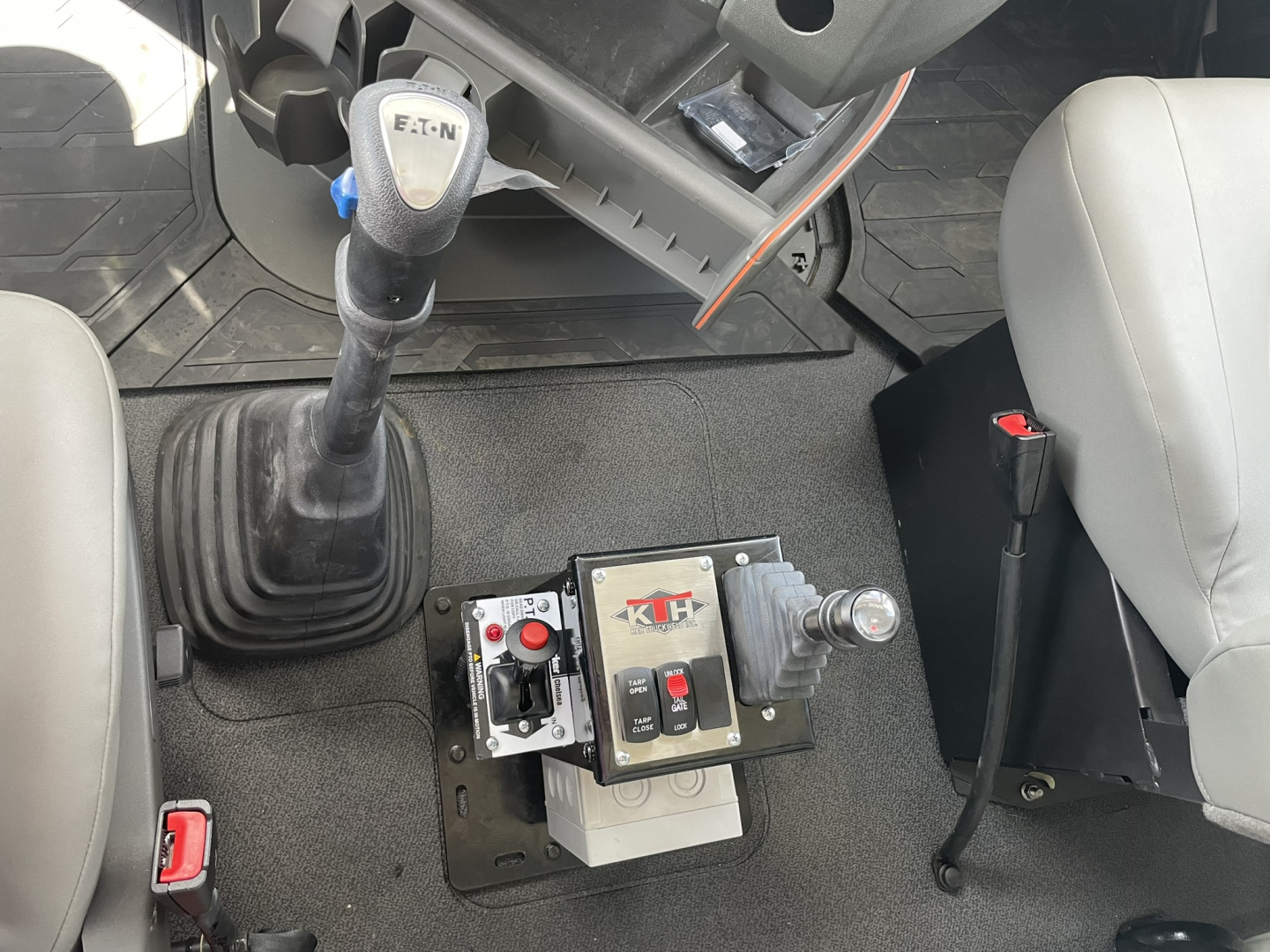 Inside cab of 2025 Volvo VHD86B300 with floor-mounted gear lever, joystick/controls, and a control box labeled XL? with red/black buttons; seating on right.