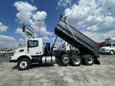Volvo VHD86B300 dump truck side view showing raised dump bed, tandem rear axles, and cab with fuel tanks.