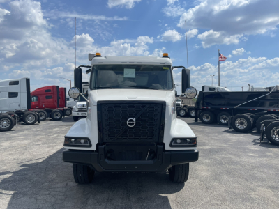 Front view of a white Volvo dump truck with large black grille, bumper, and two amber cab lights on top. Visible logo on grille.