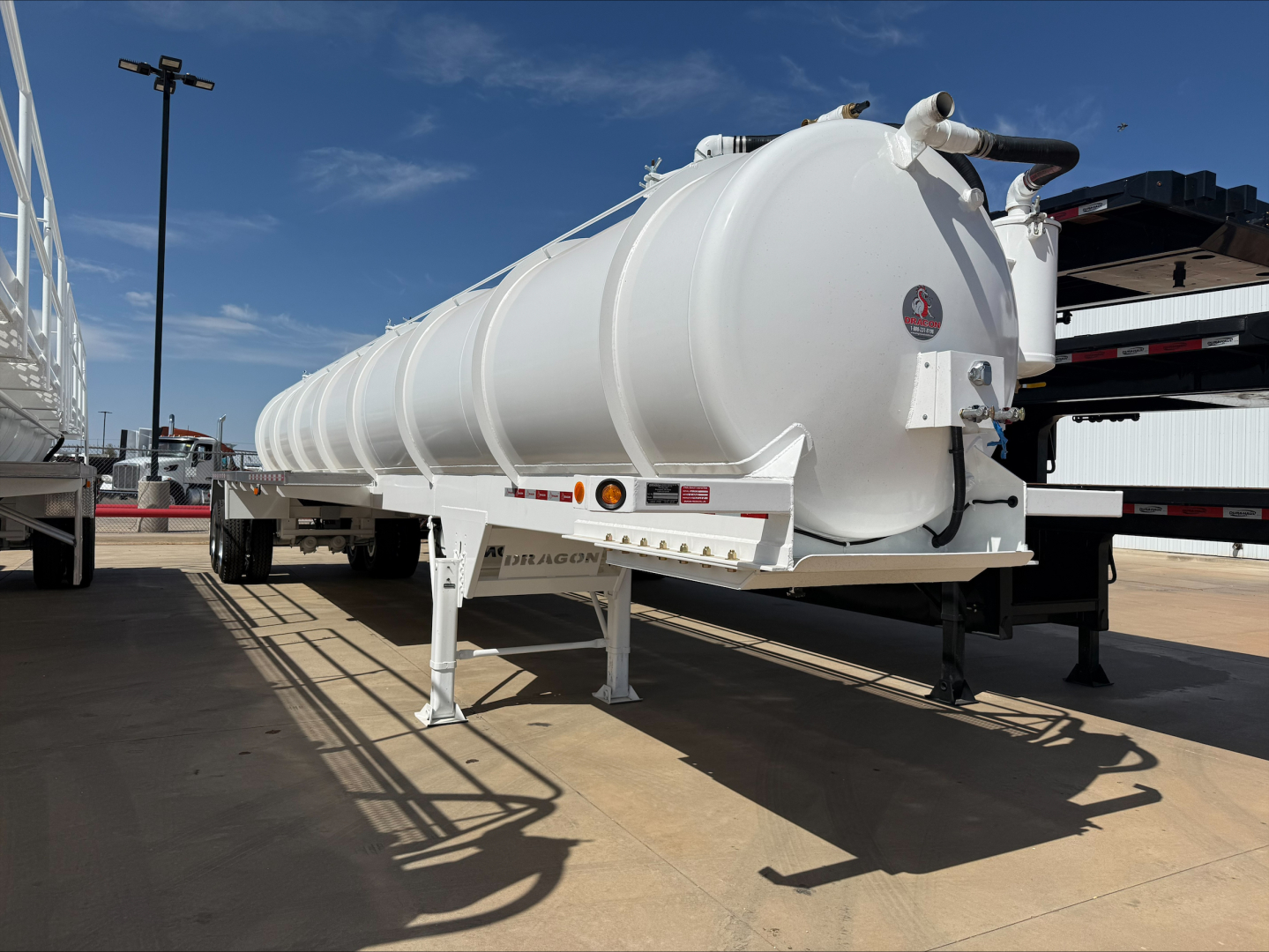 Vacuum trailer: white cylindrical tank on tandem axle with support legs, rear access hatch, and piping fittings visible.