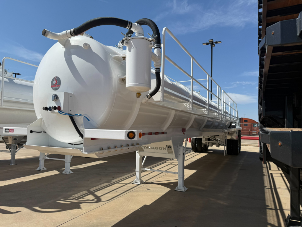 Trailer vacuum tank trailer showing white cylindrical tank with rear-mounted hoses and gauges, support legs, and safety railing; side label and scale on tank visible.